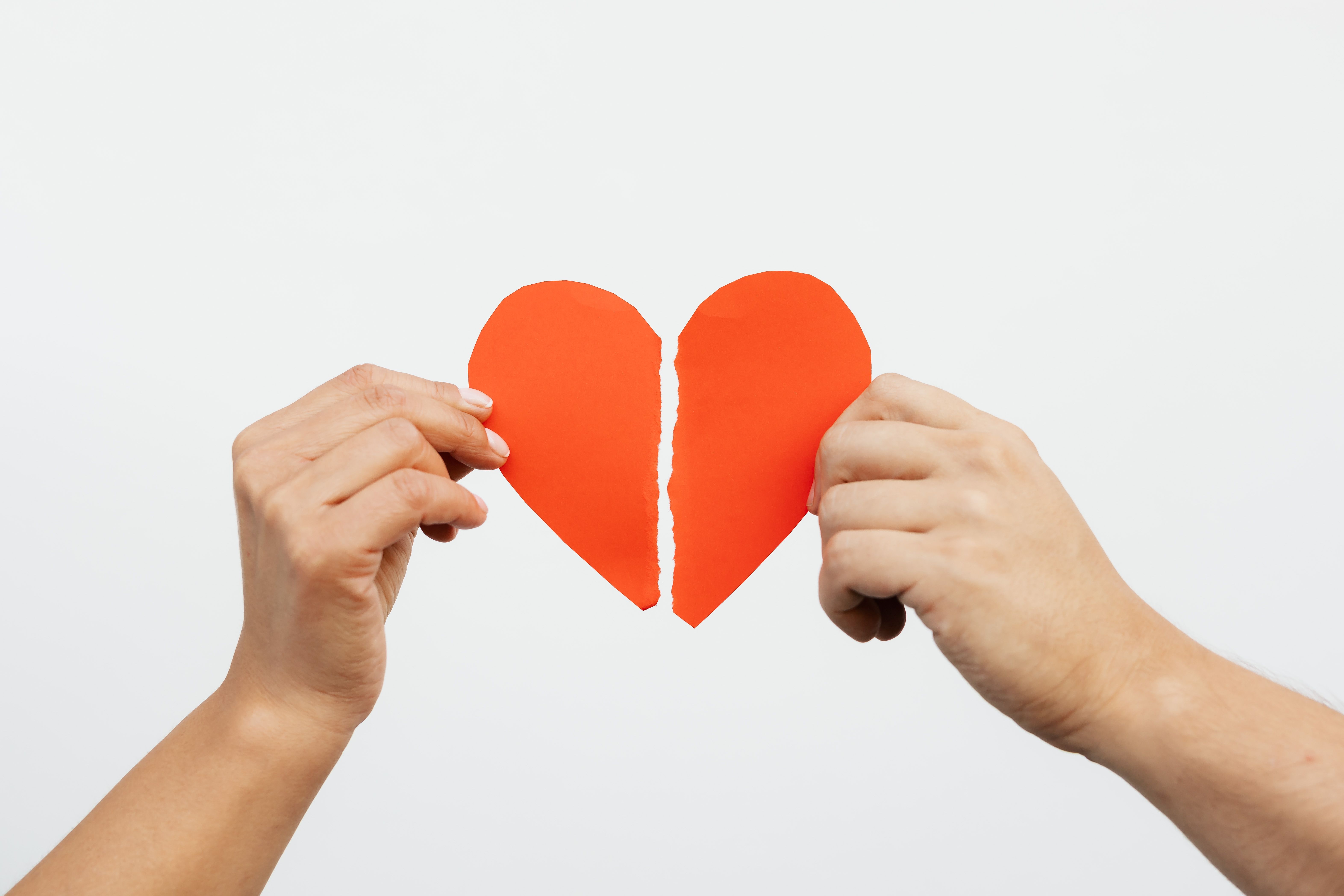 Two hands holding a torn paper heart